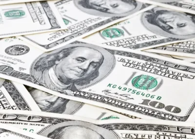 Close-up of multiple US one hundred dollar bills spread out, highlighting Benjamin Franklin's portrait and green security features.